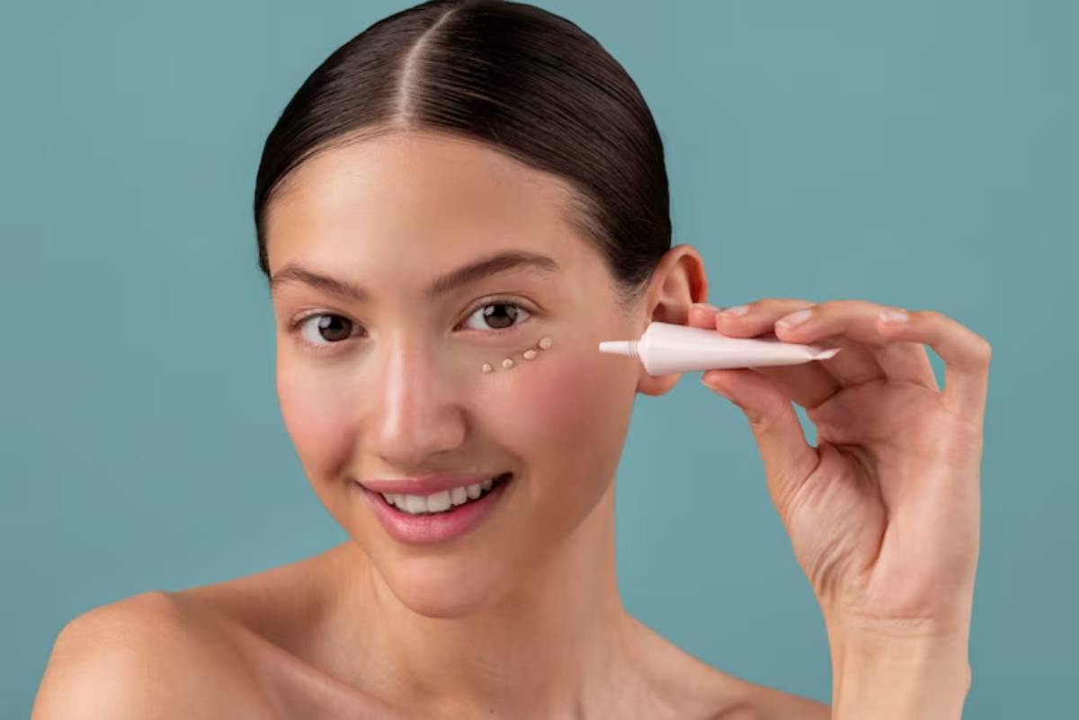 A person with sleek dark hair holds a white ear cleaning tool near their ear, set against a soft teal background.