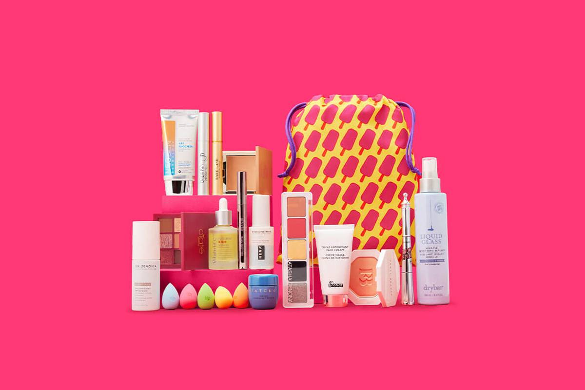A colorful assortment of beauty products including skincare, makeup, and a playful ice pop-patterned bag against a bright pink background.
