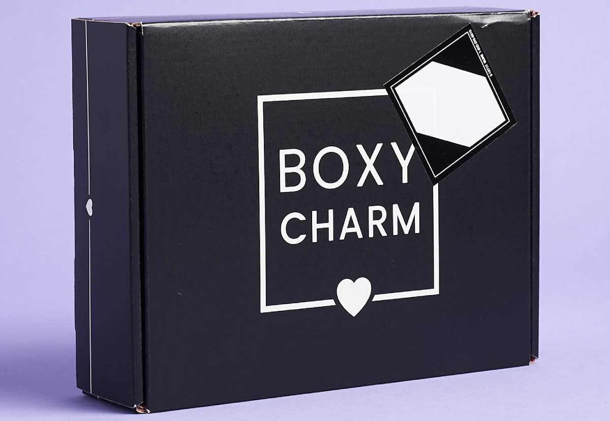 Black Boxy Charm subscription box with a white logo and heart detail, partially sealed with a blank sticker on purple background.
