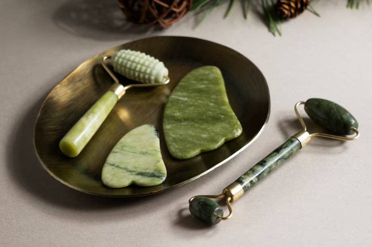 A collection of jade facial tools, including a roller and gua sha, displayed on a bronze tray against a neutral background.