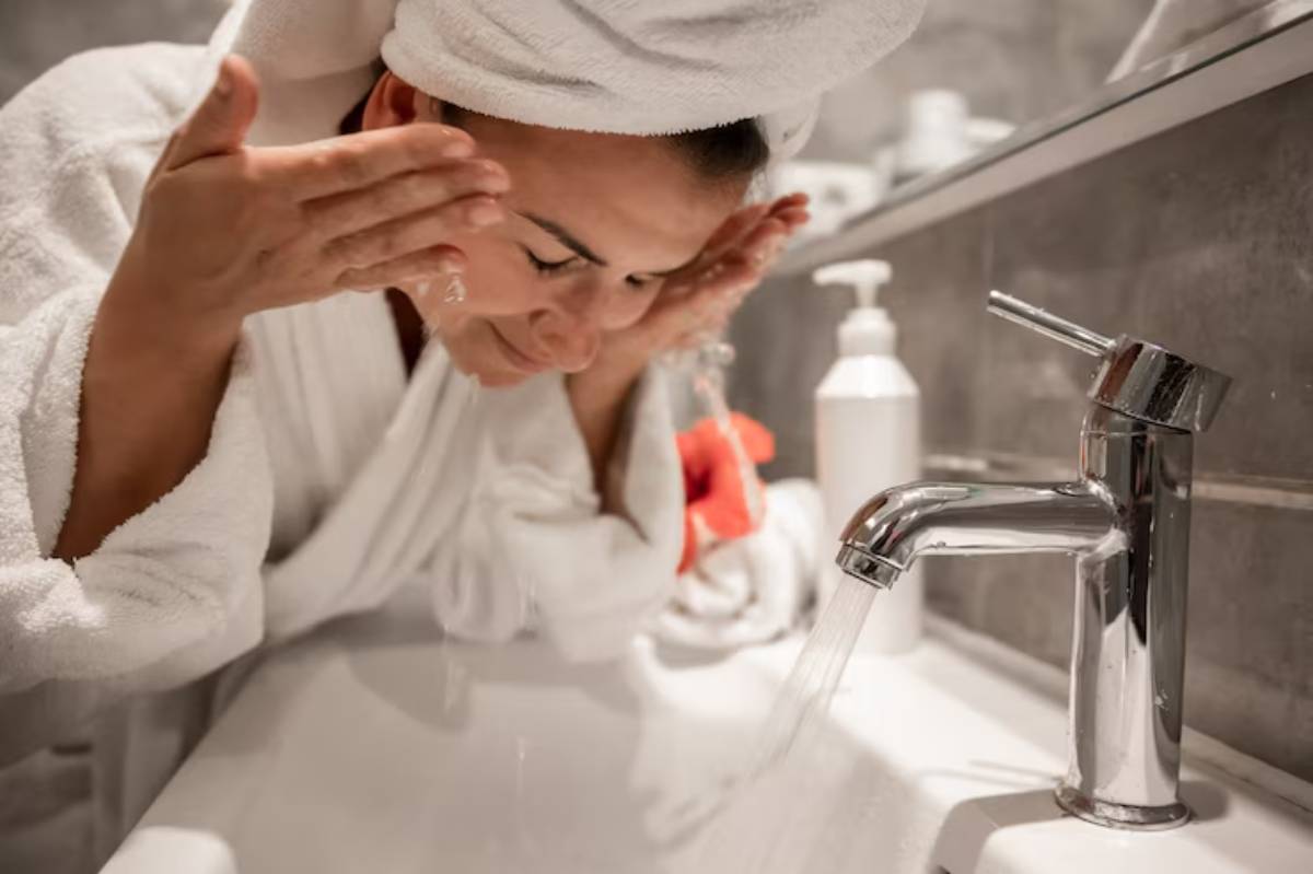 A person in a white bathrobe washes their hands over a stylish bathroom sink, with toiletries visible in the background.