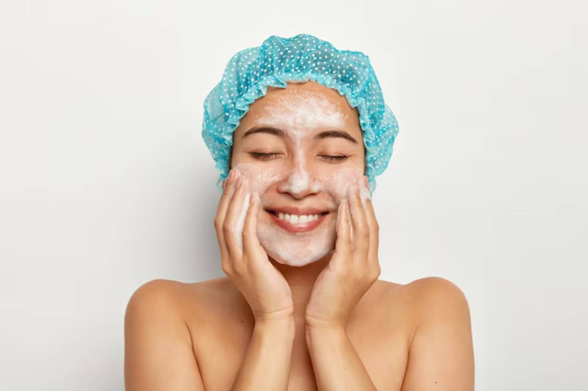 A person wearing a blue polka-dotted shower cap holds their hands on either side of their face against a plain white background.