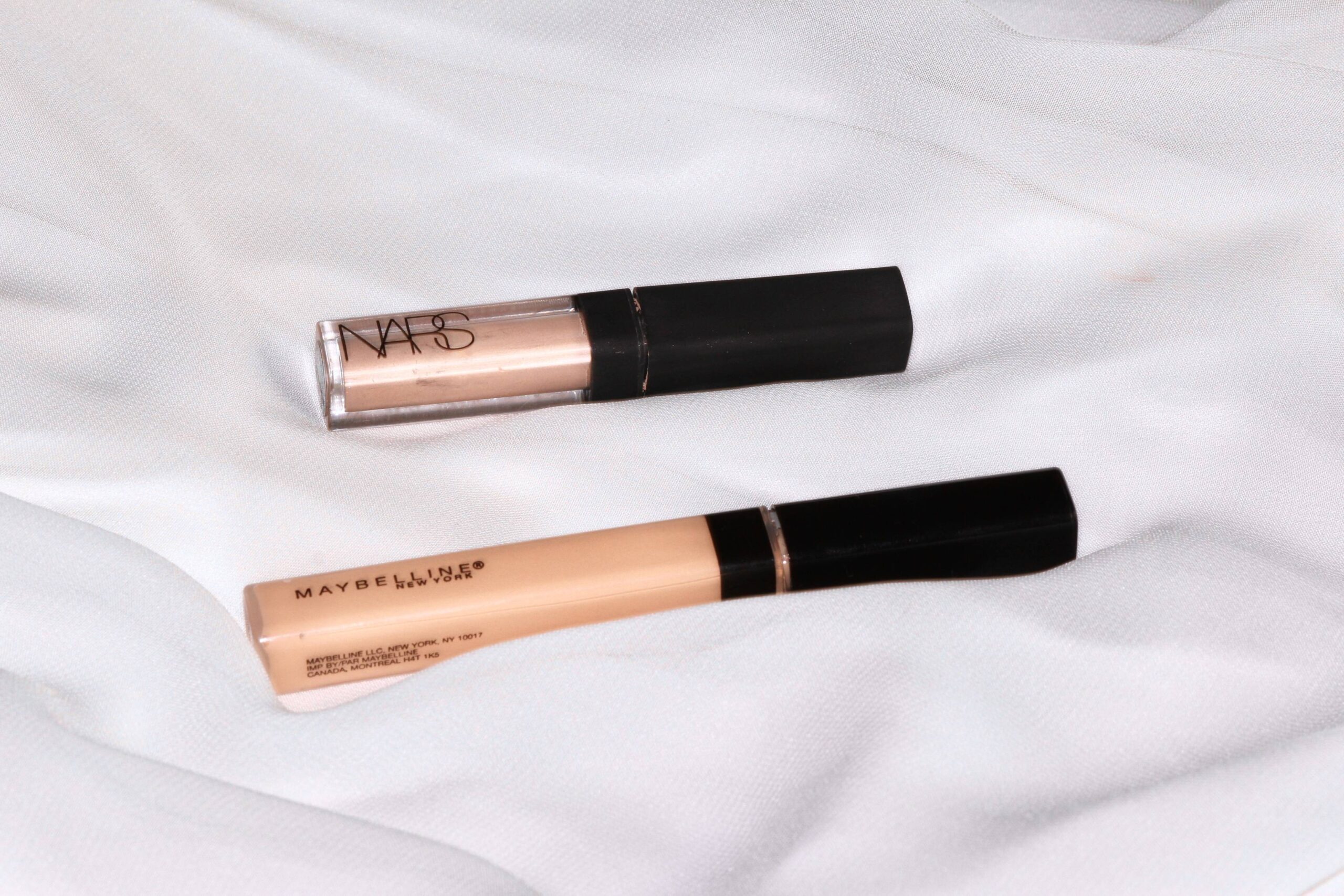 Two concealers, one from NARS and the other from Maybelline, resting on a soft white fabric background.