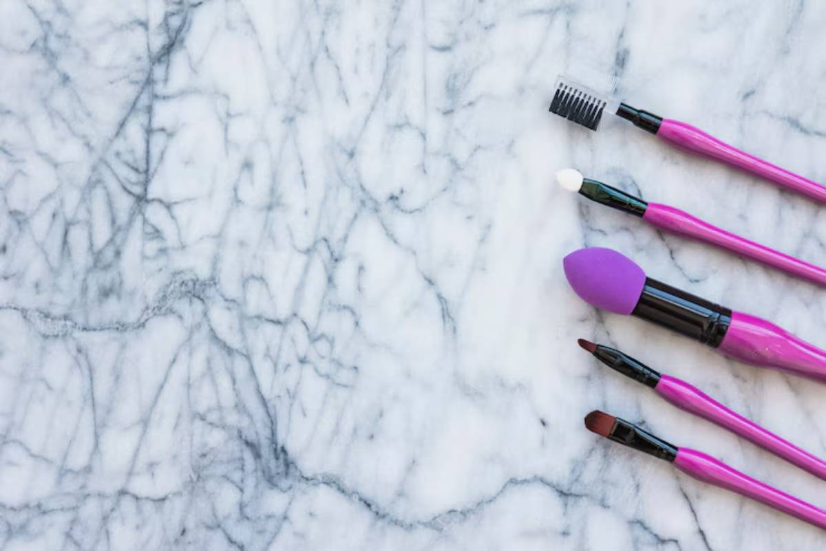Five colorful makeup brushes arranged on a marble countertop, featuring varied brush heads for diverse cosmetic applications.