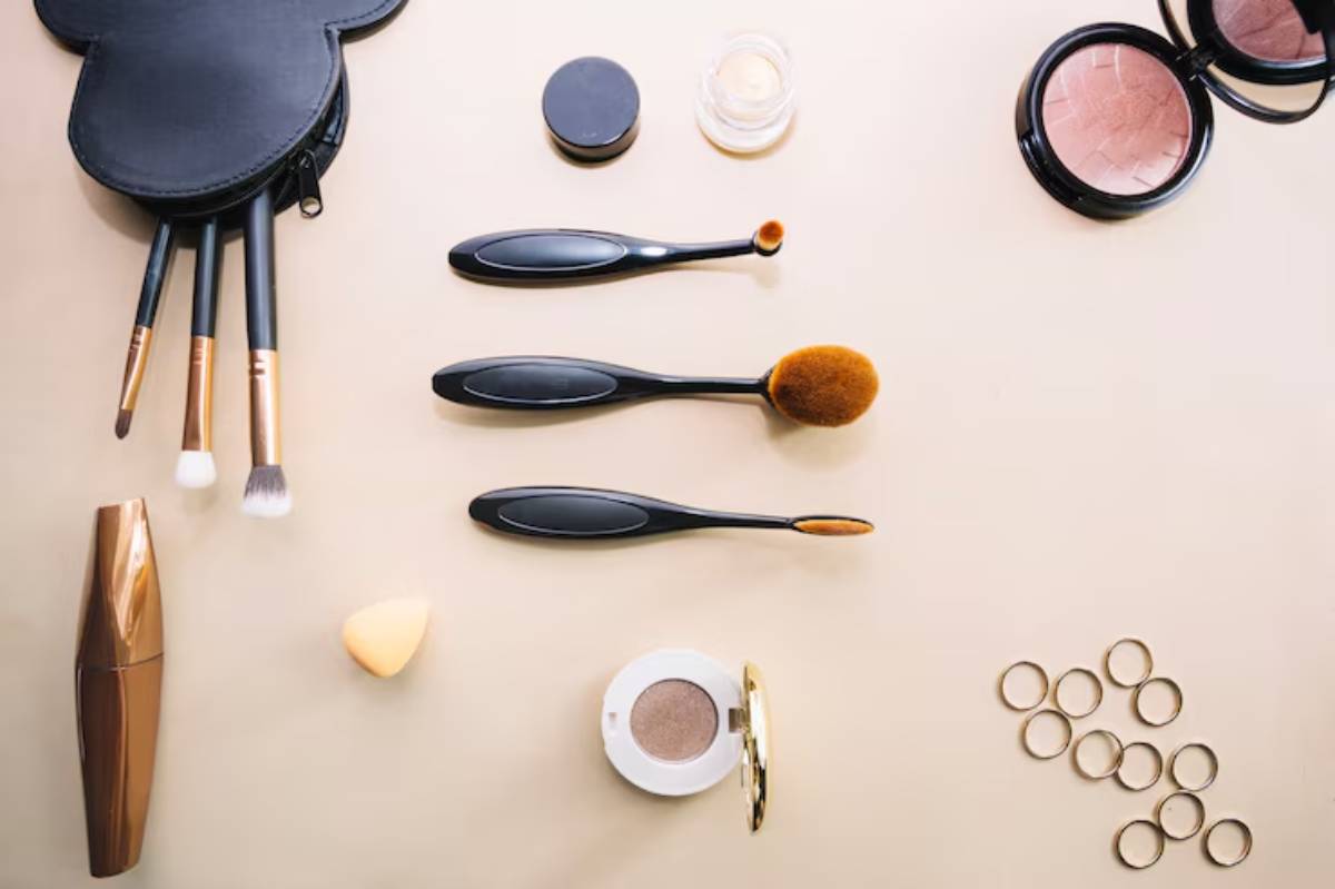 An arrangement of makeup tools, including brushes, a sponge, mascara, and eyeshadow, set against a soft beige background.
