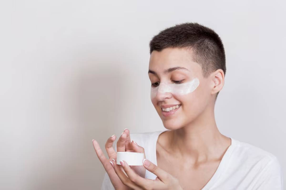 A person in a white shirt holds a small jar, appearing engaged in a skincare routine against a light gray background.