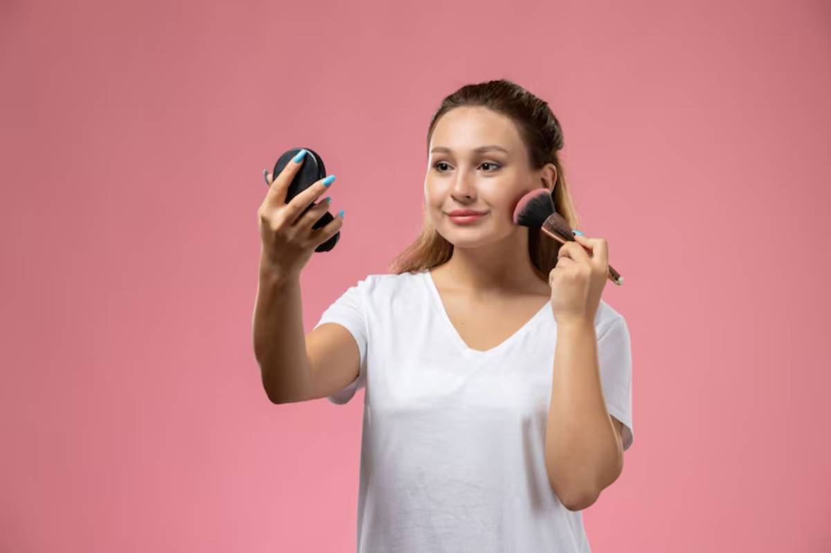 A person scrolling through an online makeup store on a smartphone, surrounded by various cosmetics and credit cards on a wooden table.