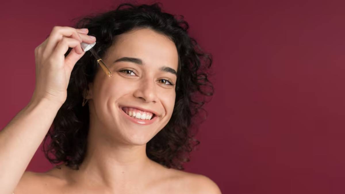 A person with curly hair holds a cotton pad, preparing for a skincare routine against a deep red background.