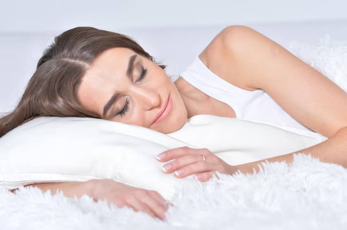 A woman rests her head on a soft white pillow, surrounded by fluffy bedding, exuding a cozy and relaxed atmosphere.