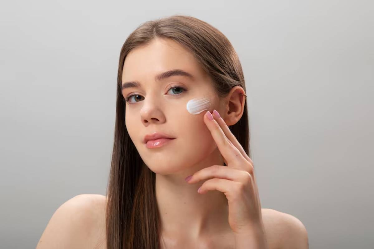 A woman with long, straight hair rests her chin on her hand, against a neutral gray background.