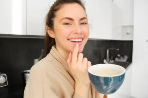 A person holding a blue bowl in a modern kitchen, wearing a beige robe, with a sleek black countertop in the background.