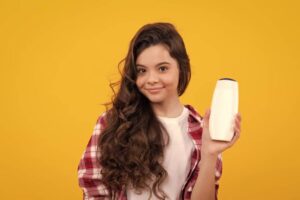 A person in a plaid shirt holds a white bottle against a bright yellow background, showcasing hair care or beauty product.