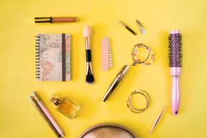 Flat lay of beauty and travel items on a bright yellow background: cosmetics, a map notebook, jewelry, and tools.
