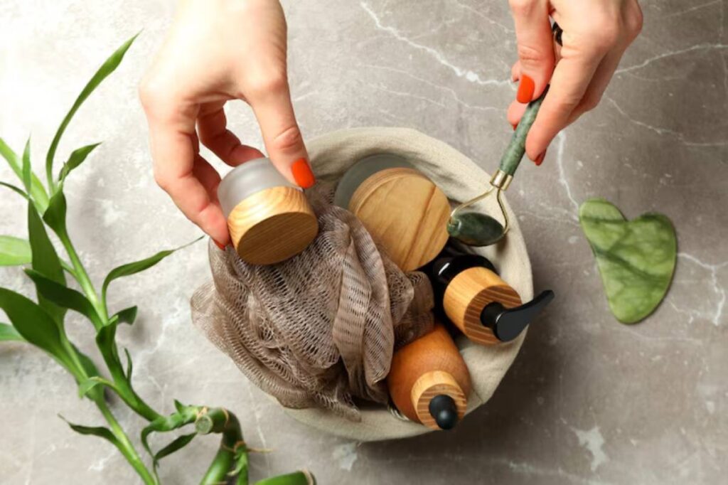 A hand reaches for a glass jar from a soft beige bowl filled with skincare products and a jade roller, surrounded by green leaves.
