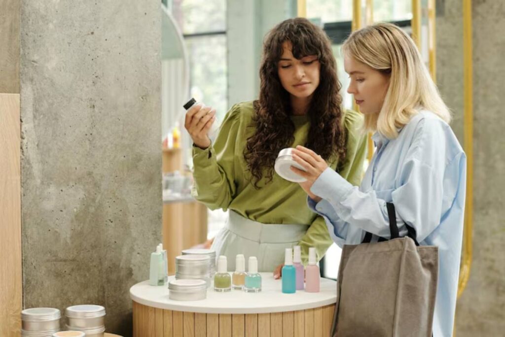 Two women are examining cosmetic products on a circular display table in a modern store, surrounded by natural light and concrete walls.